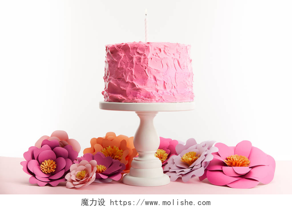 白色背景墙一个粉色桌子的蛋糕和粉色花朵粉红色的生日蛋糕与蜡烛在蛋糕立场附近的纸花隔离在白色